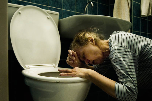 Eine Frau kniet im Badezimmer über der Toilette, die Stirn auf den Arm gelehnt.